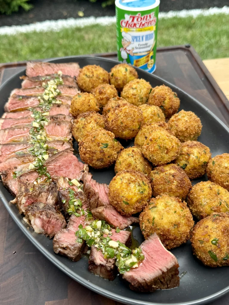 Complete steakhouse dinner showing sliced ribeye with herb garnish alongside golden crispy croquettes on black plate with Tony's seasoning