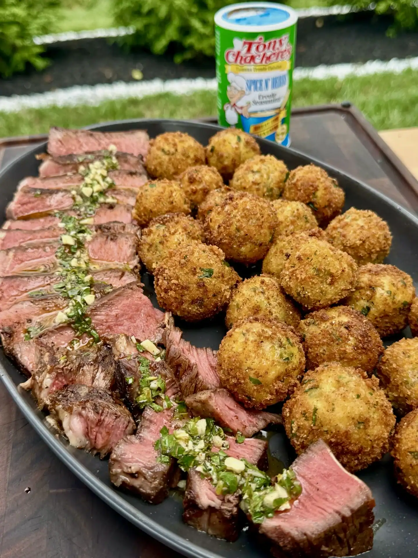 Complete steakhouse dinner showing sliced ribeye with herb garnish alongside golden crispy croquettes on black plate with Tony's seasoning