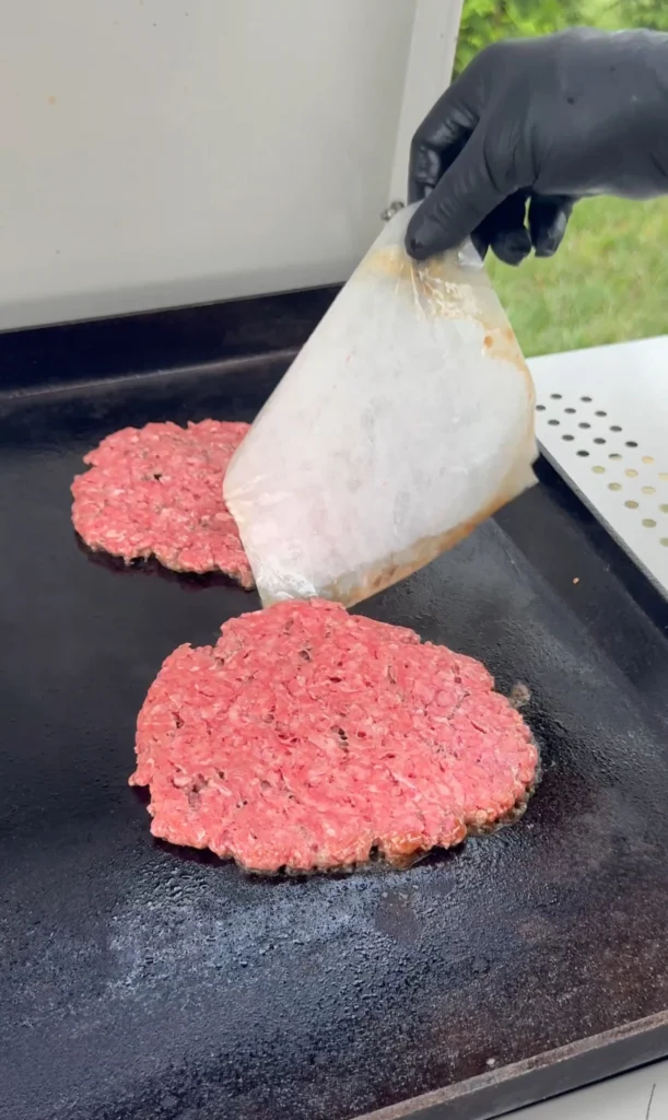 smash burger on the griddle with wax paper being lifted