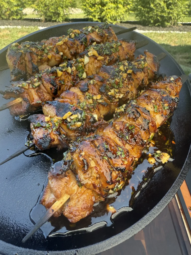 up close on 4 chicken skewers on a black plate