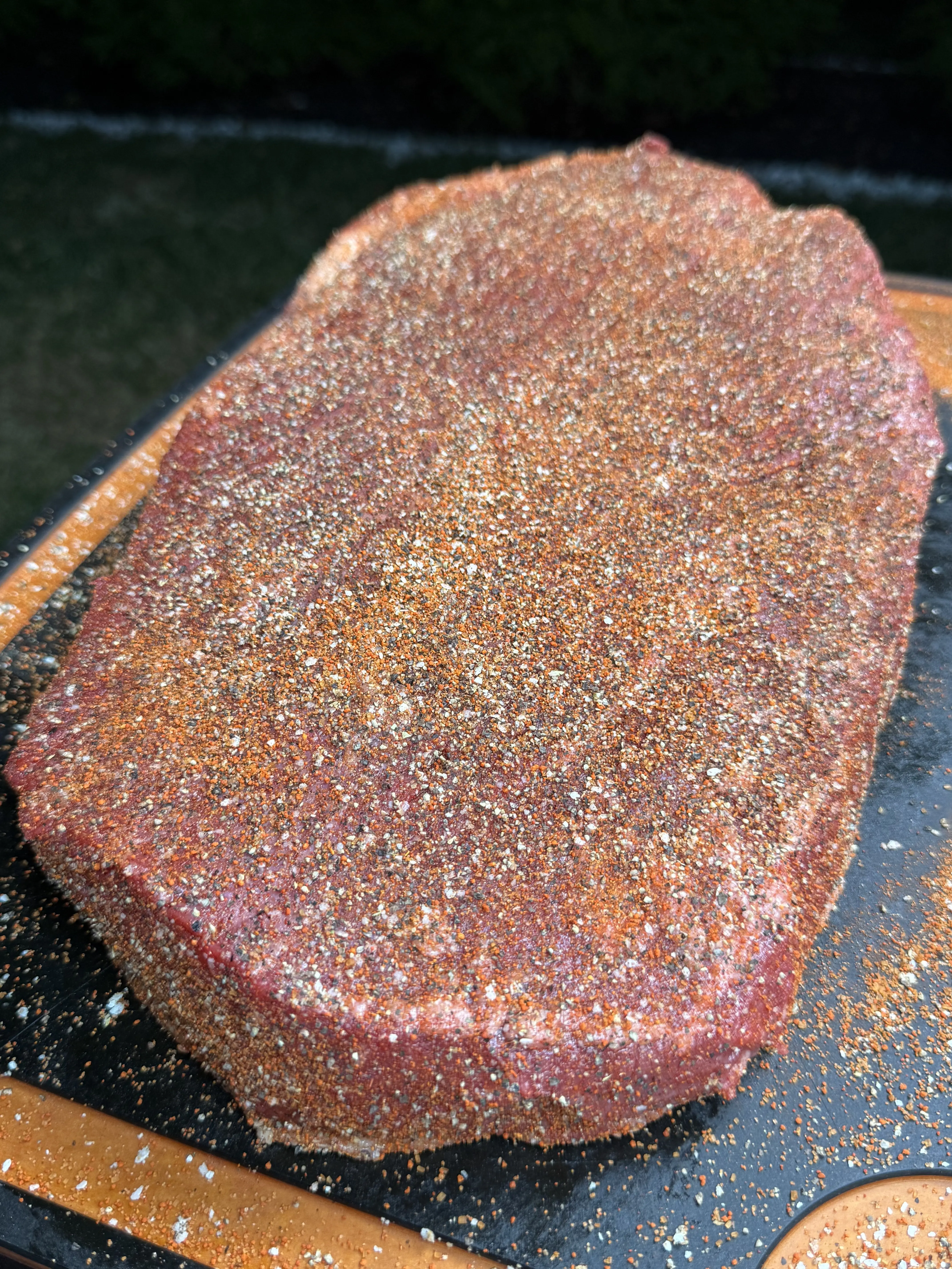 Coarse salt pepper and garlic powder being applied to brisket before smoking