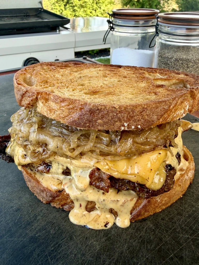 finalized patty melt on a cutting board with salt and pepper in the background