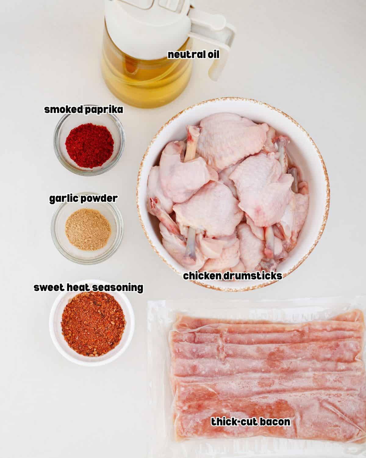 Ingredients for bacon wrapped chicken lollipops including chicken drumsticks, bacon, BBQ seasoning, garlic powder, smoked paprika, and oil