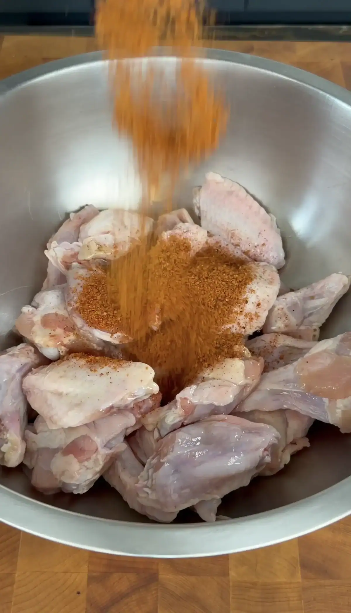 raw chicken wings in a stainless steel being seasoned.