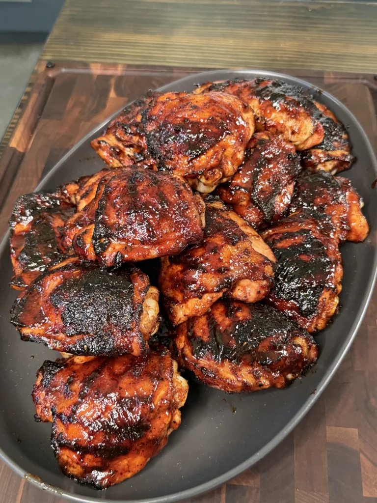 Grilled bone-in chicken thighs resting on a wooden cutting board with fresh lime squeezed over top