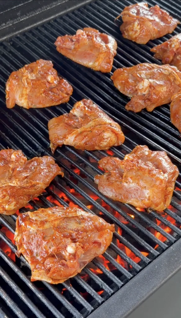 Bone-in chicken thighs searing skin-side down over direct heat with visible char marks forming