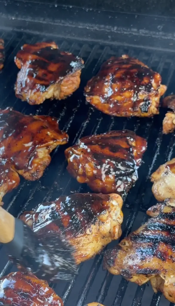 Bone-in chicken thighs searing skin-side down over direct heat with visible char marks forming