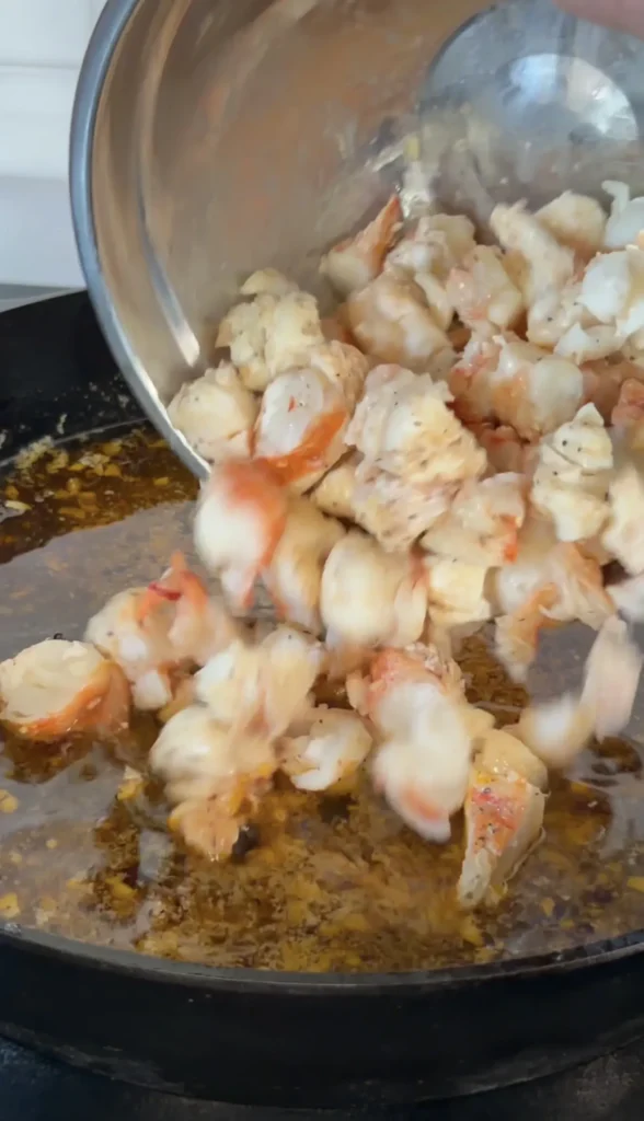 Fresh cooked lobster meat being poured from a pot into a sizzling pan with butter for hot honey butter lobster rolls