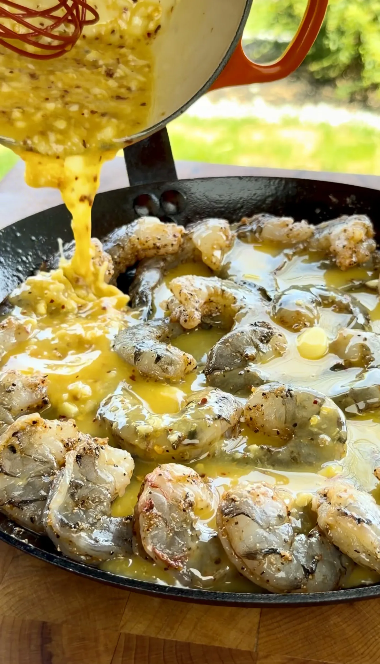 Garlic butter sauce being poured over shrimp in a cast iron skillet
