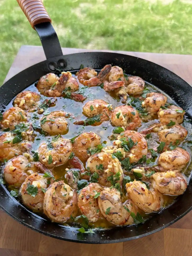 Golden seared shrimp with garlic butter and fresh herbs cooking in a black cast iron skillet