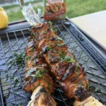 Grilled marinated chicken skewers with fresh herbs on a wire cooling rack next to grilled corn and onions