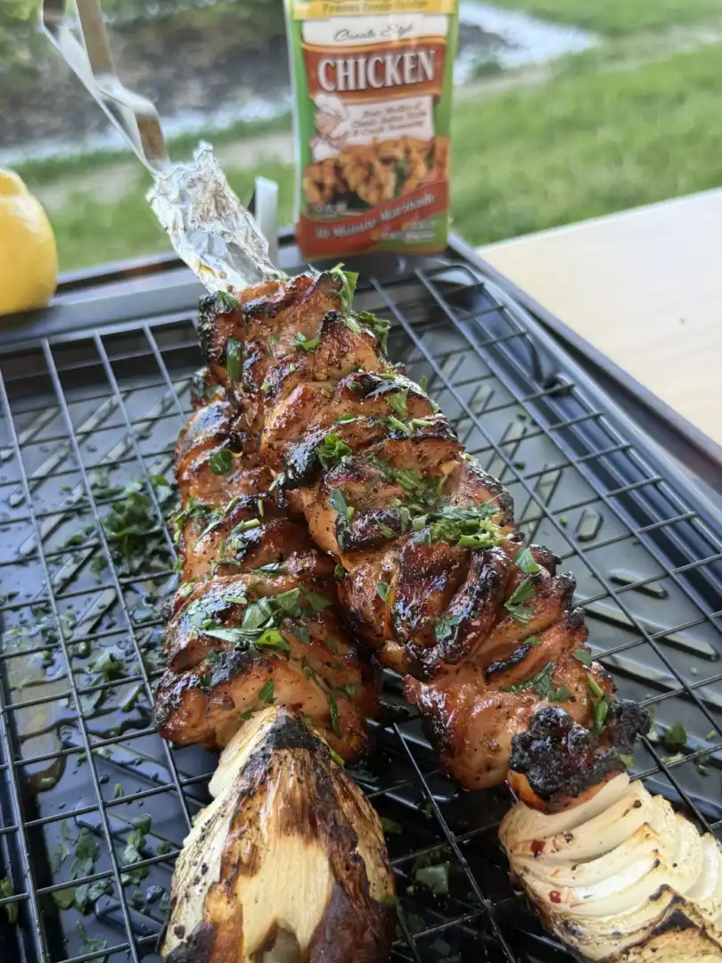 Grilled marinated chicken skewers with fresh herbs on a wire cooling rack next to grilled corn and onions