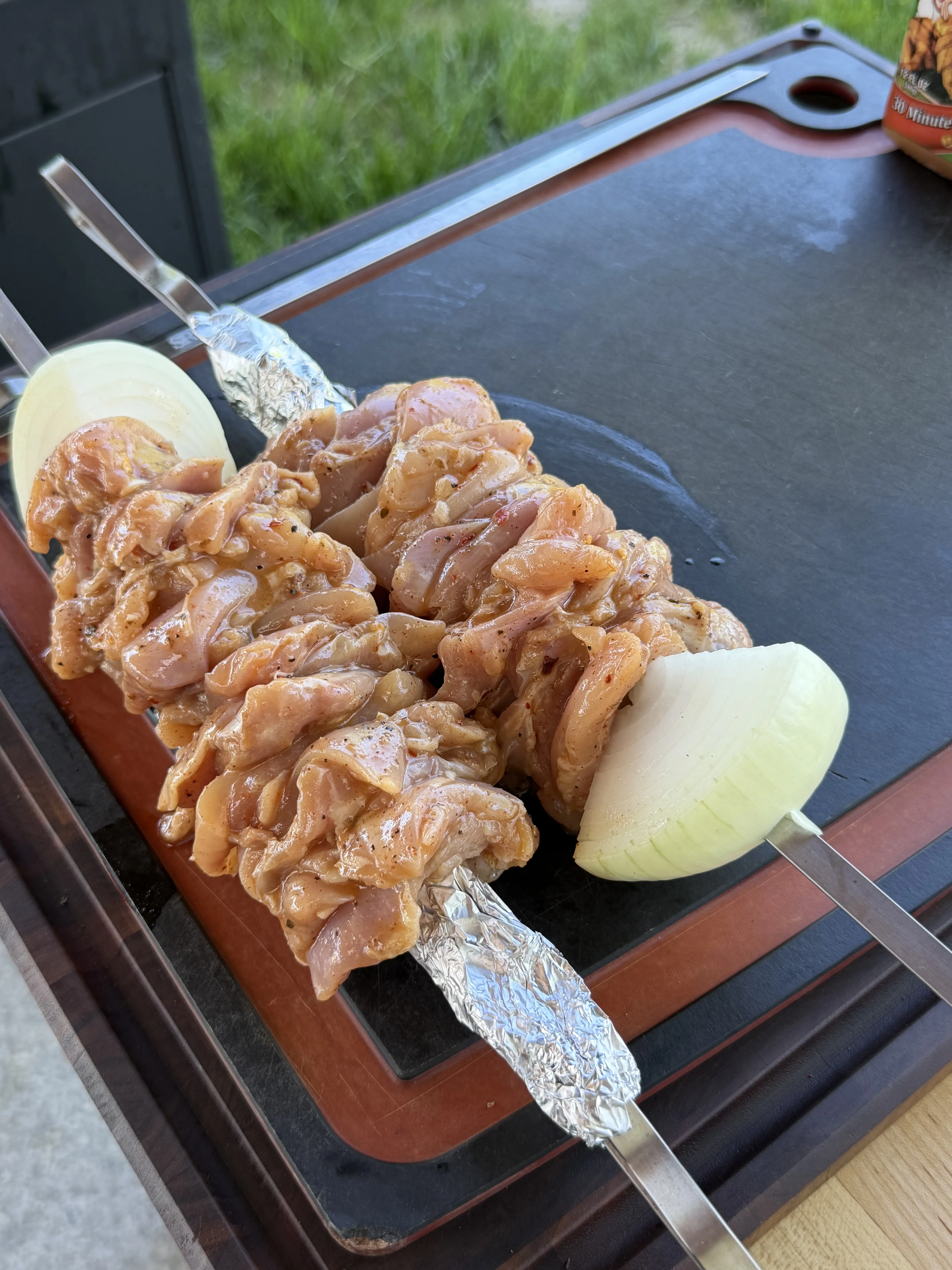 Finished grilled chicken thigh skewers resting on a slate serving board with fresh herbs