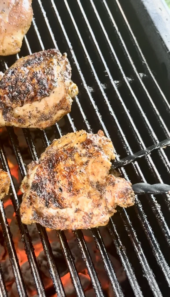 Golden brown honey chili crisp chicken thighs with crispy seasoned skin cooking on black grill grates over flames