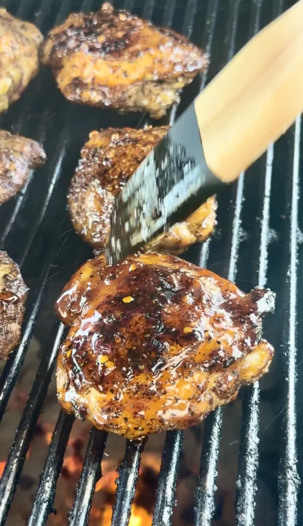 Honey chili crisp chicken thighs with caramelized glaze cooking on grill grates over flames