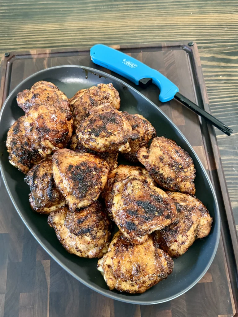 Honey chili crisp grilled chicken thighs with caramelized coating arranged in a dark pan on wooden cutting board