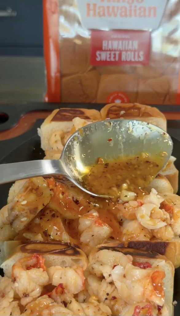 Hot honey butter lobster rolls with golden sauce being drizzled from a spoon, Hawaiian sweet rolls in background