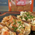 Hot honey butter lobster rolls on dark plate, topped with fresh chives and caramelized onions