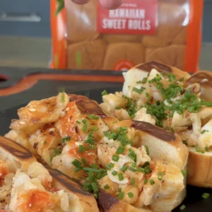 Hot honey butter lobster rolls on dark plate, topped with fresh chives and caramelized onions