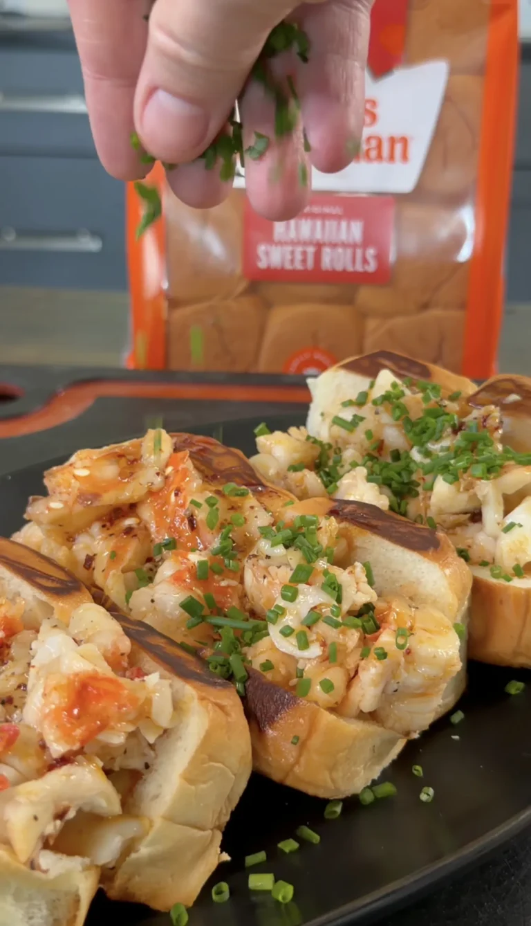 Hot honey butter lobster rolls on dark plate, topped with fresh chives and caramelized onions