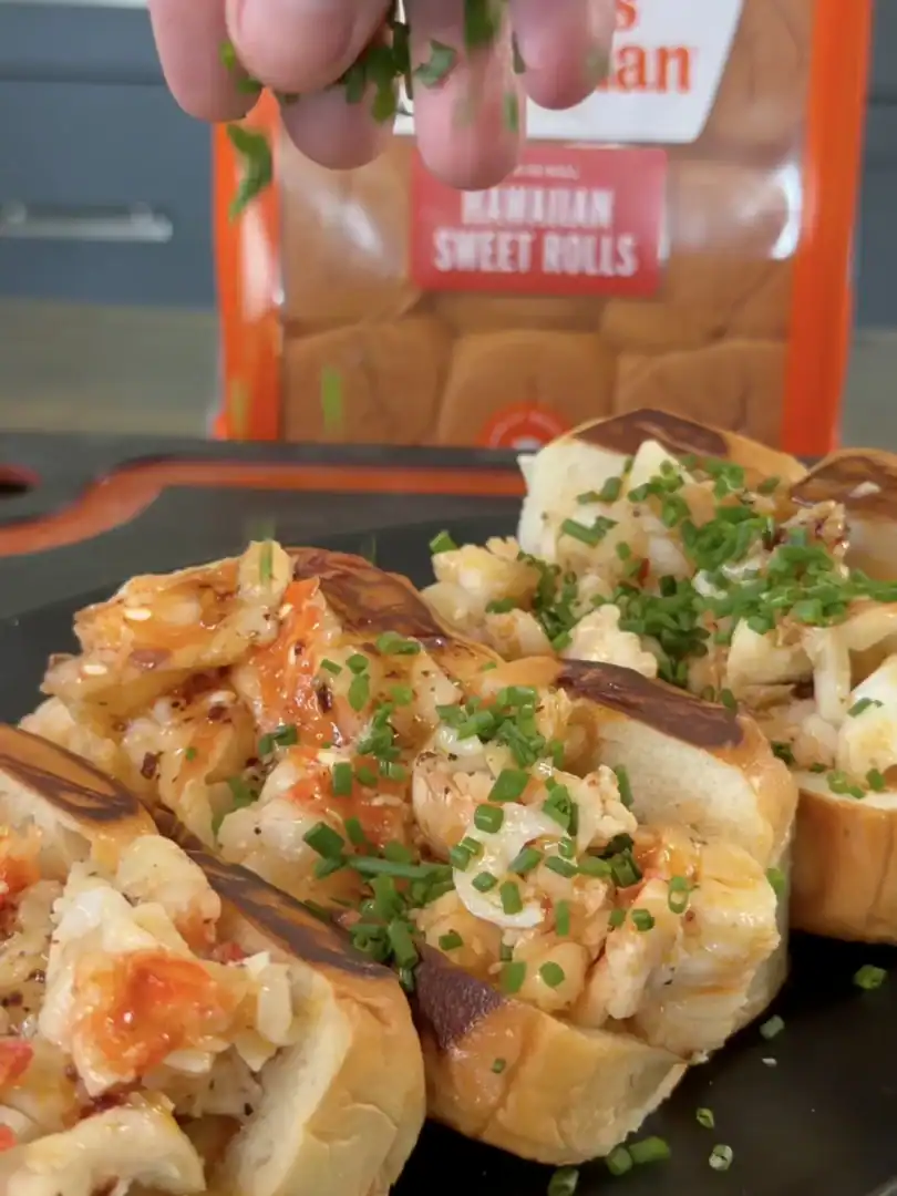 Hot honey butter lobster rolls on dark plate, topped with fresh chives and caramelized onions