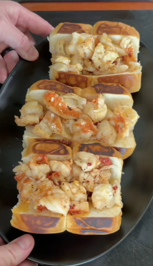 Three hot honey butter lobster rolls with chunks of lobster meat on golden brioche buns served on black plate