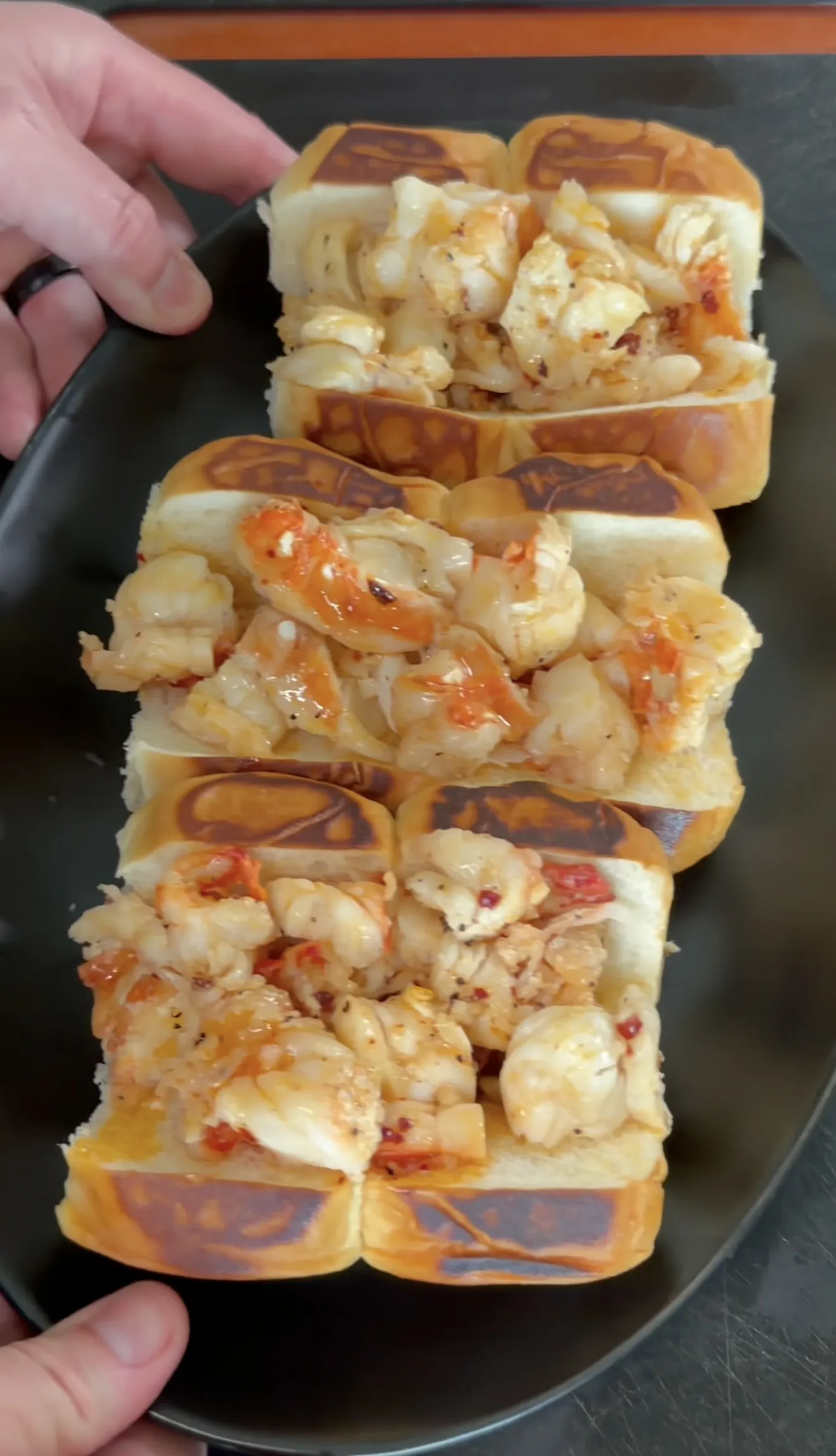 Three hot honey butter lobster rolls with chunks of lobster meat on golden brioche buns served on black plate