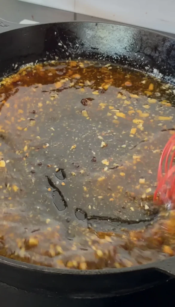Lobster pieces cooking in bubbling hot honey butter sauce in a large black skillet