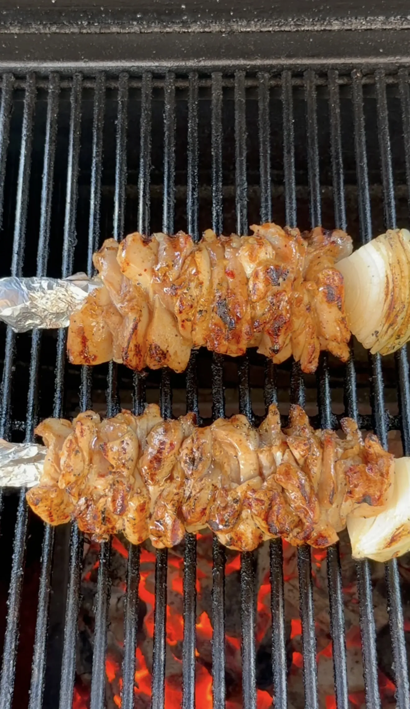 Marinated chicken skewers grilling on BBQ grates with visible grill marks and golden color