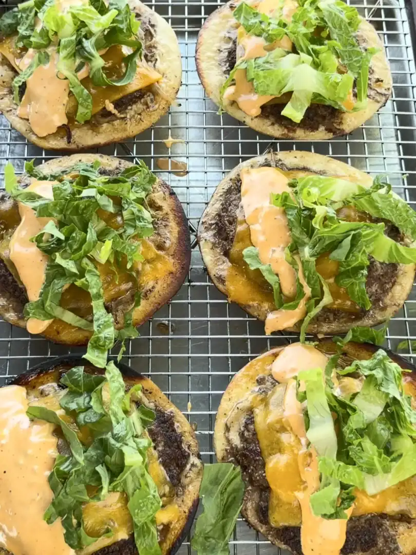 Six Oklahoma onion smash burger tacos with melted cheese, lettuce and sauce cooling on wire rack