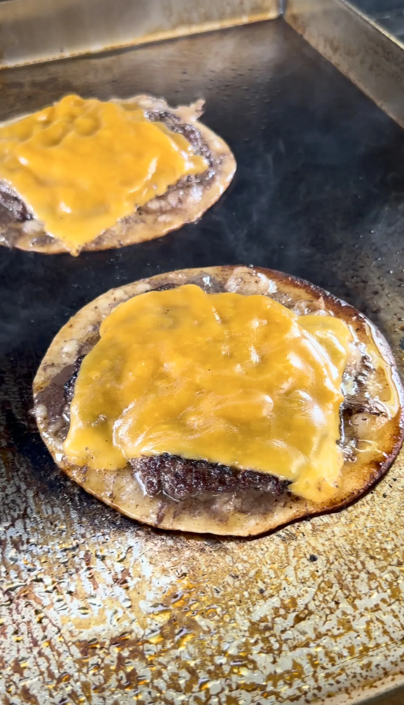 Oklahoma onion smash burger tacos cooking on the griddle with melted cheese
