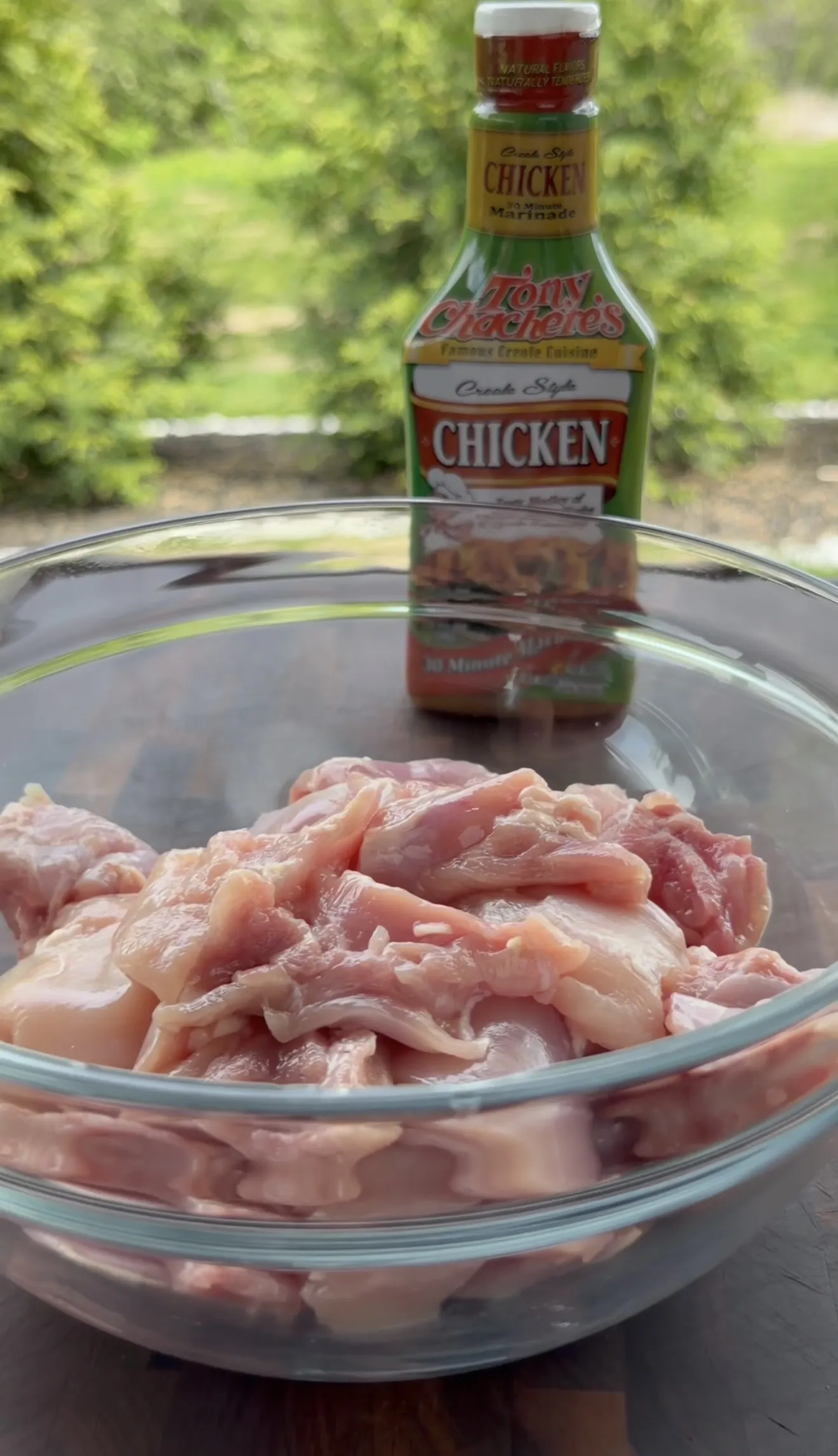 Tony Chachere's Creole-Style Chicken Marinade being added to raw chicken strips in a glass bowl