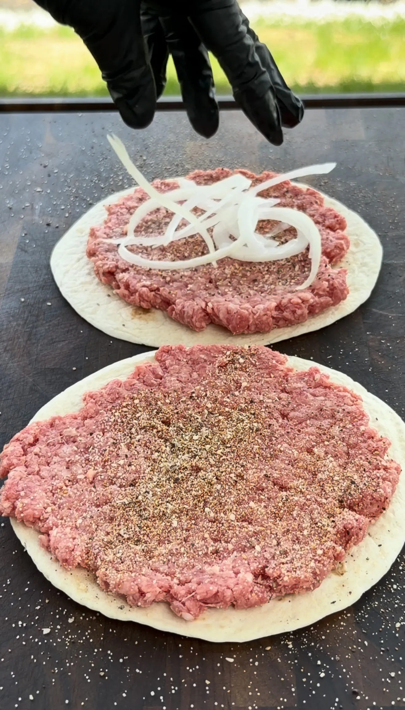 Raw ground beef portioned onto street taco flour tortillas with onions ready for the griddle