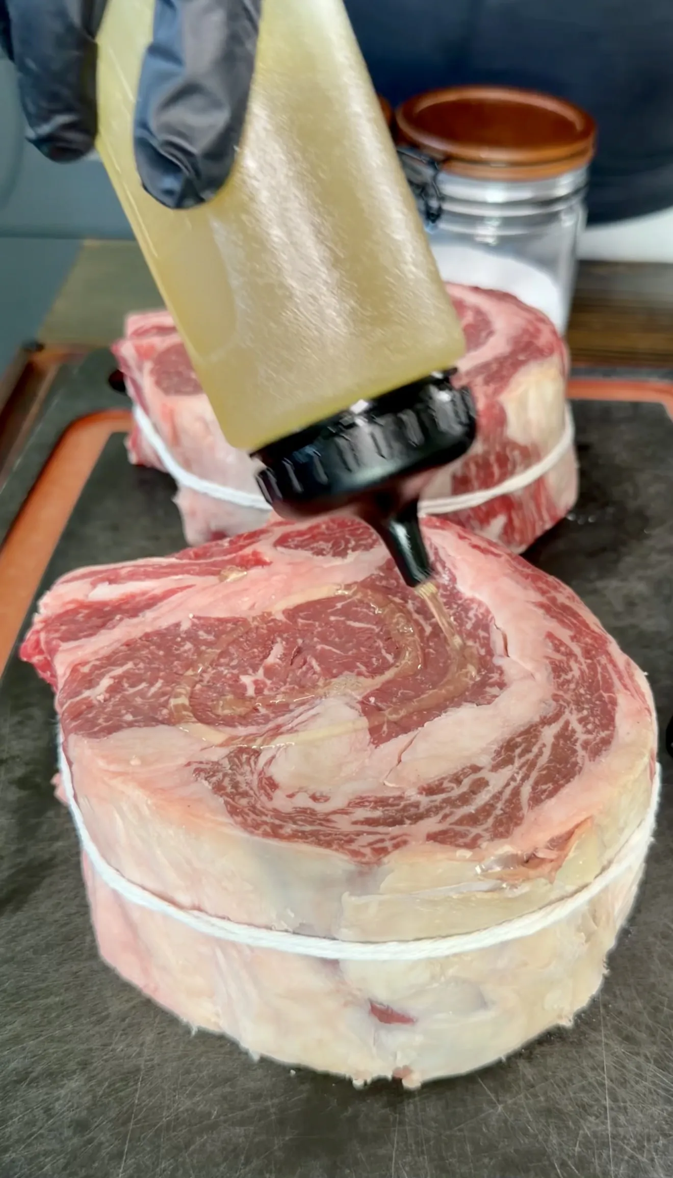 Raw ribeye steaks being seasoned during preparation