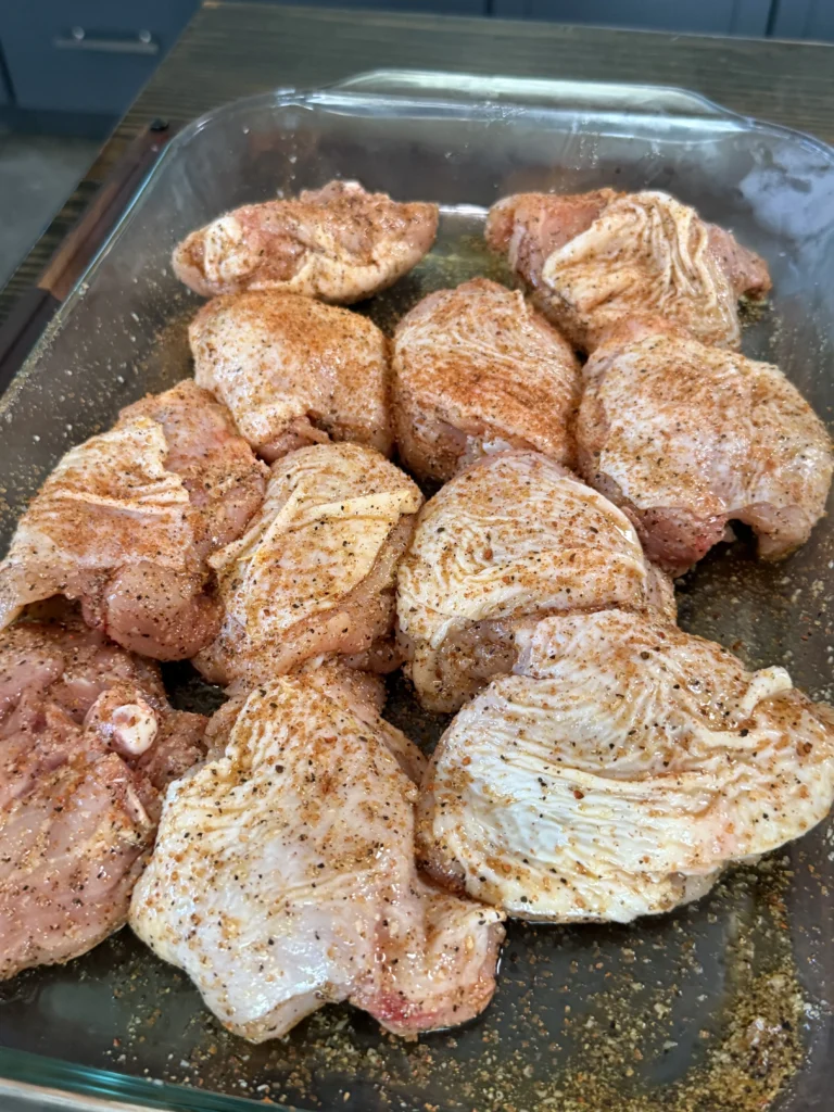 Raw chicken thighs seasoned with spices in a clear glass baking dish, ready for honey chili crisp preparation