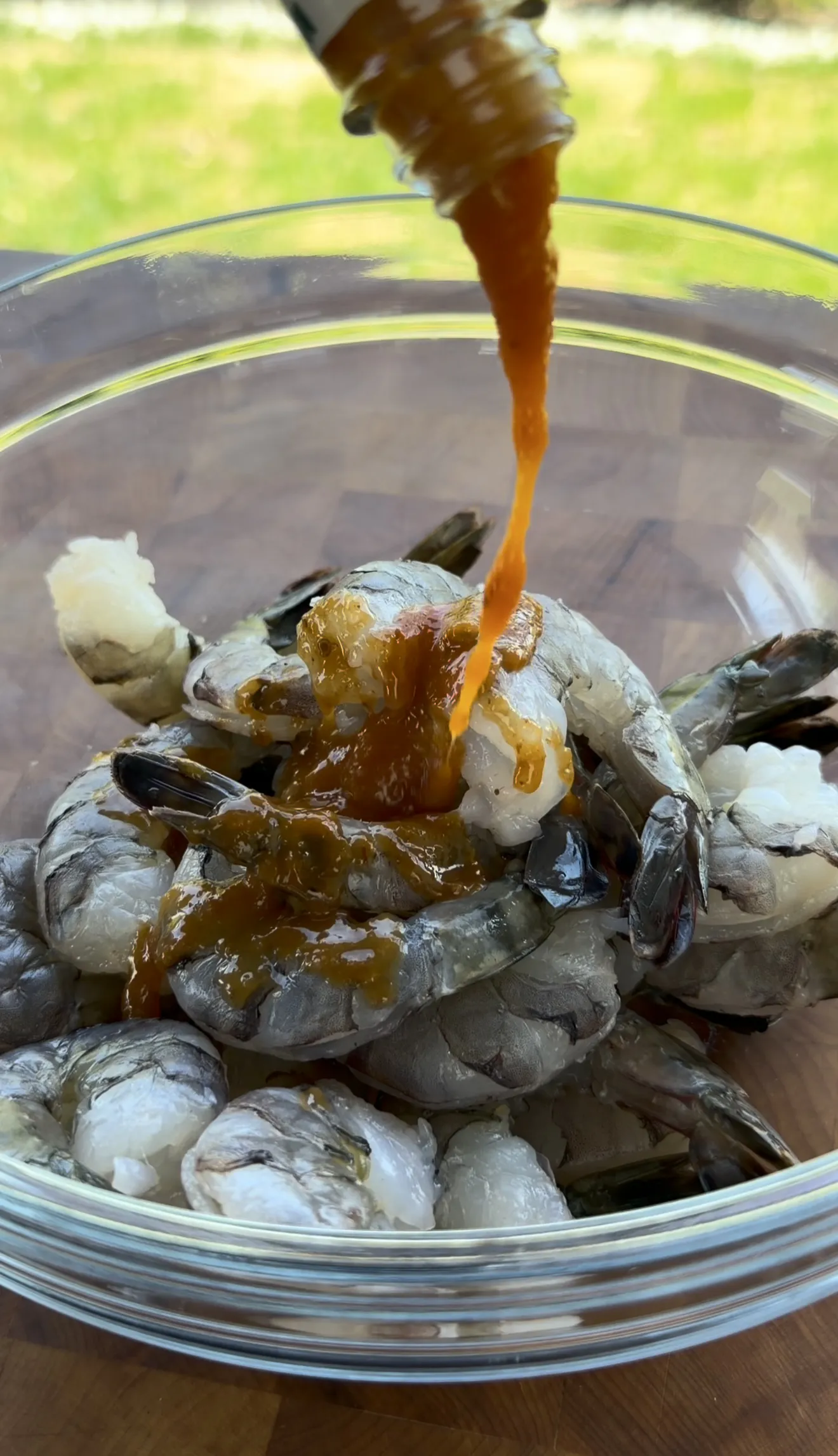 Raw shrimp coated with garlic butter marinade in a glass bowl