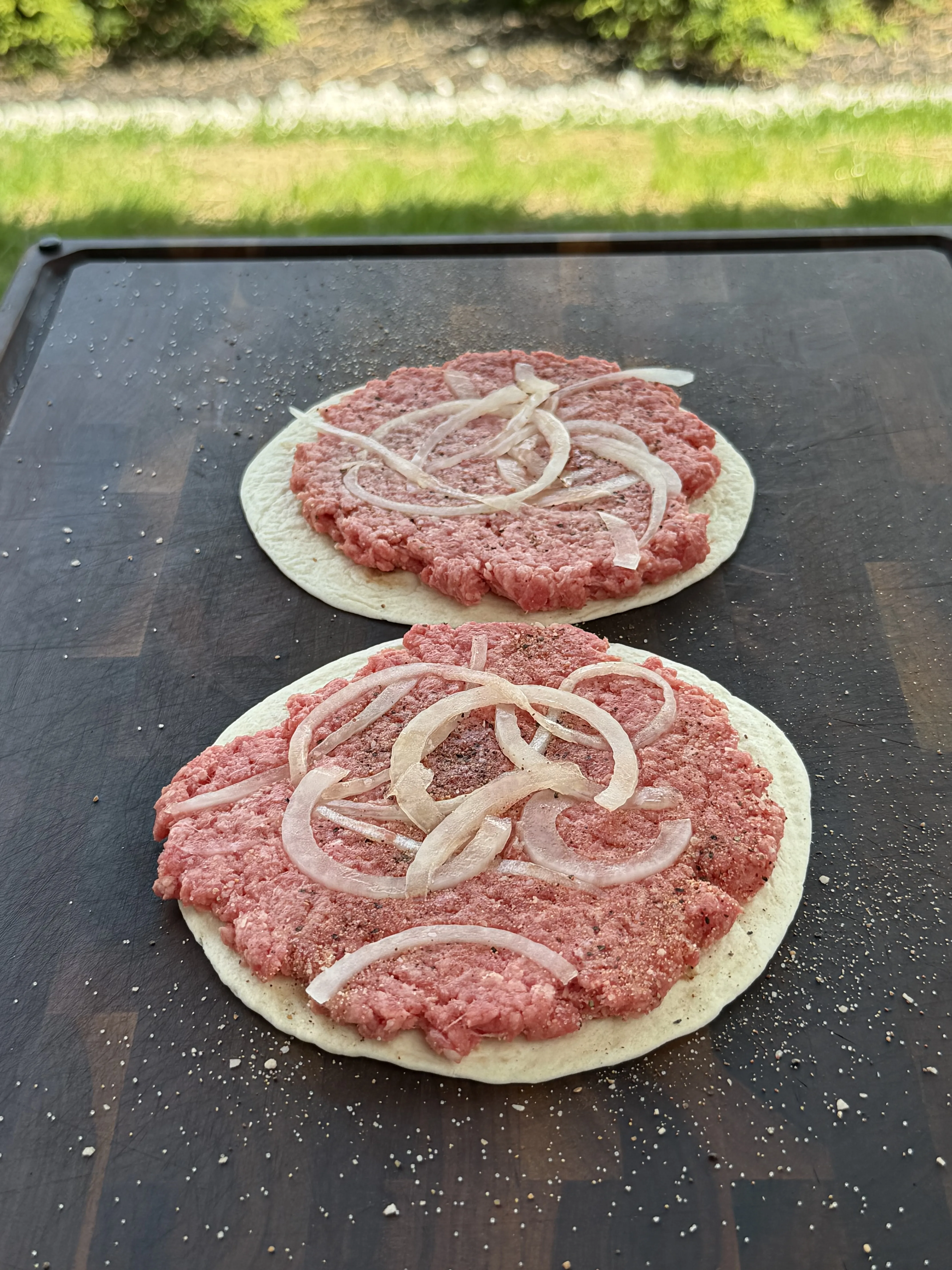 Raw smash burger taco patties topped with paper-thin onions pressed into the beef
