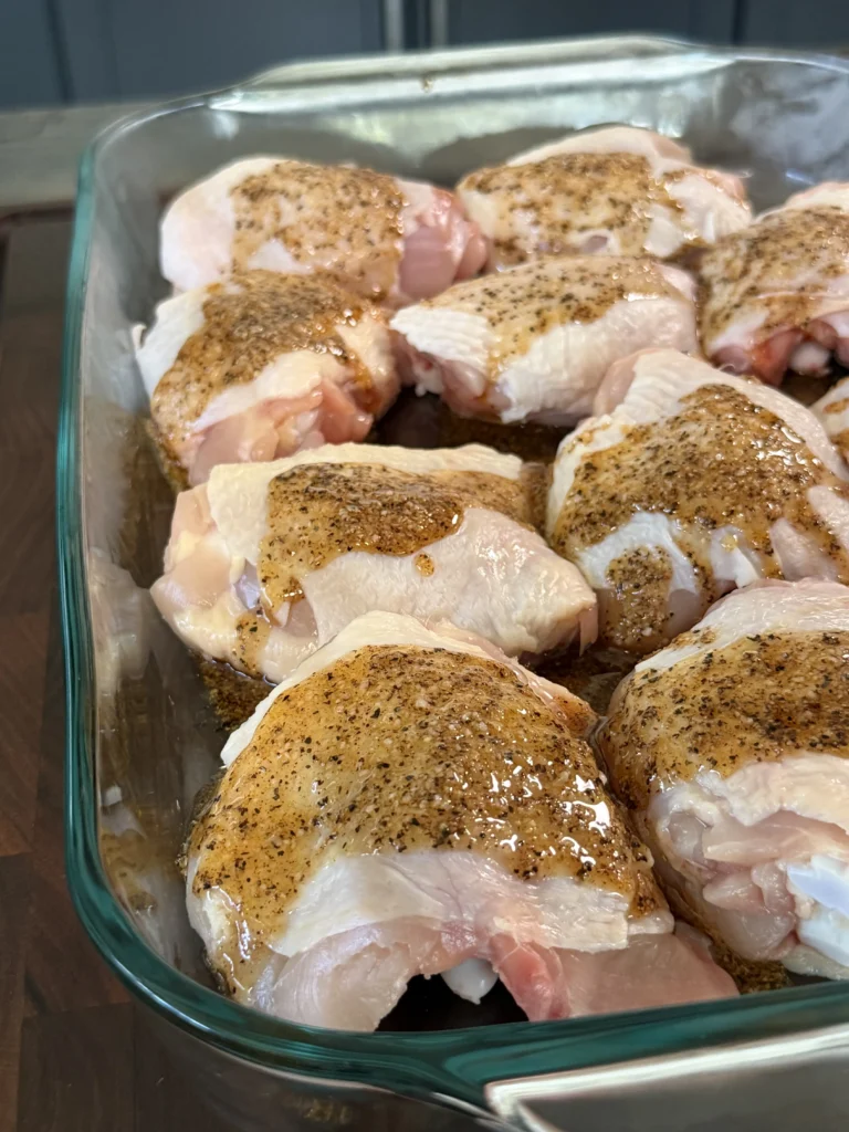 Raw chicken thighs seasoned with spices and honey chili crisp marinade arranged in a clear glass baking dish