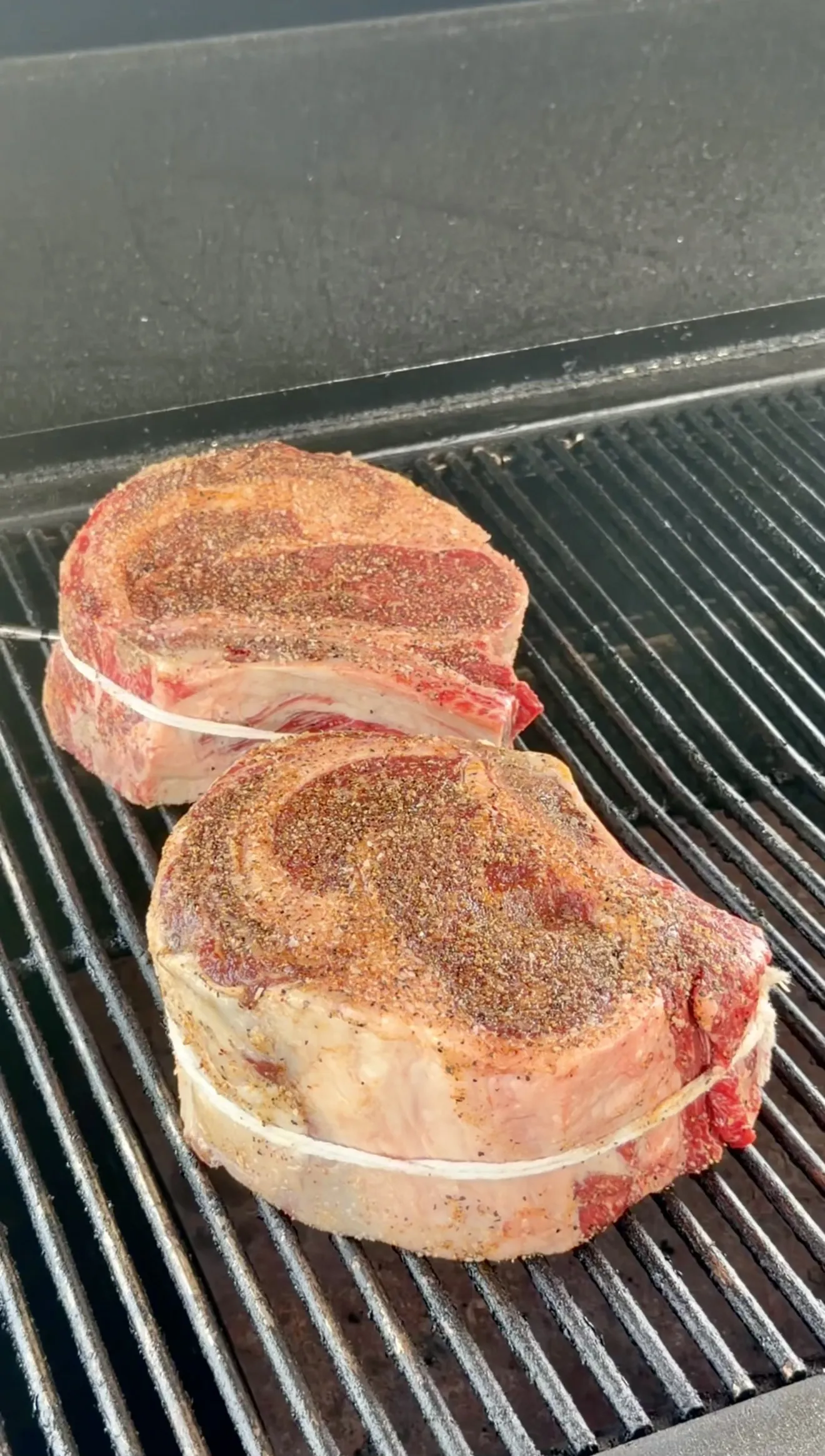 Seasoned ribeye steaks placed on grill grates for smoking