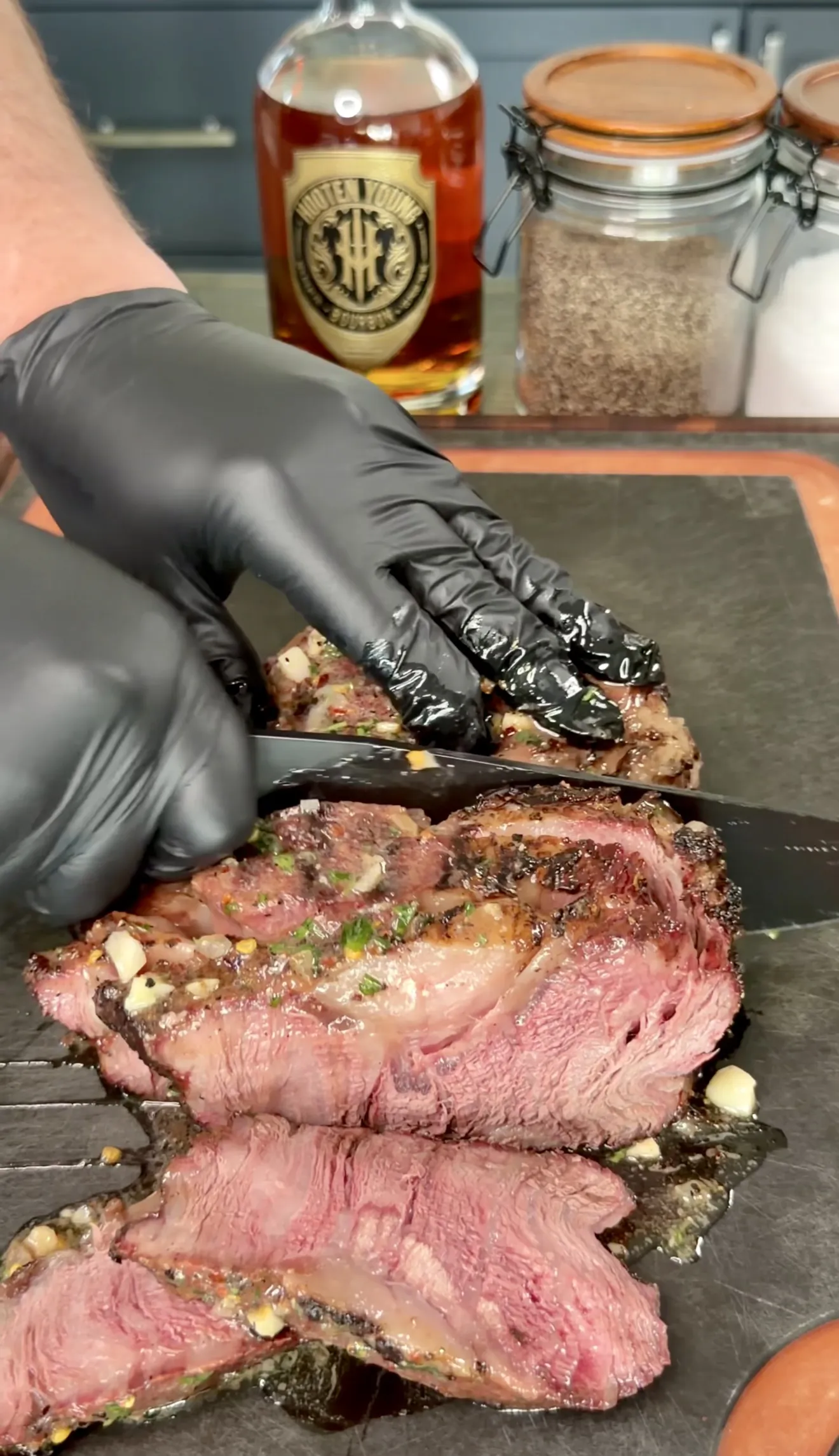 Sliced grilled steak with whiskey butter on a cutting board showing medium-rare interior