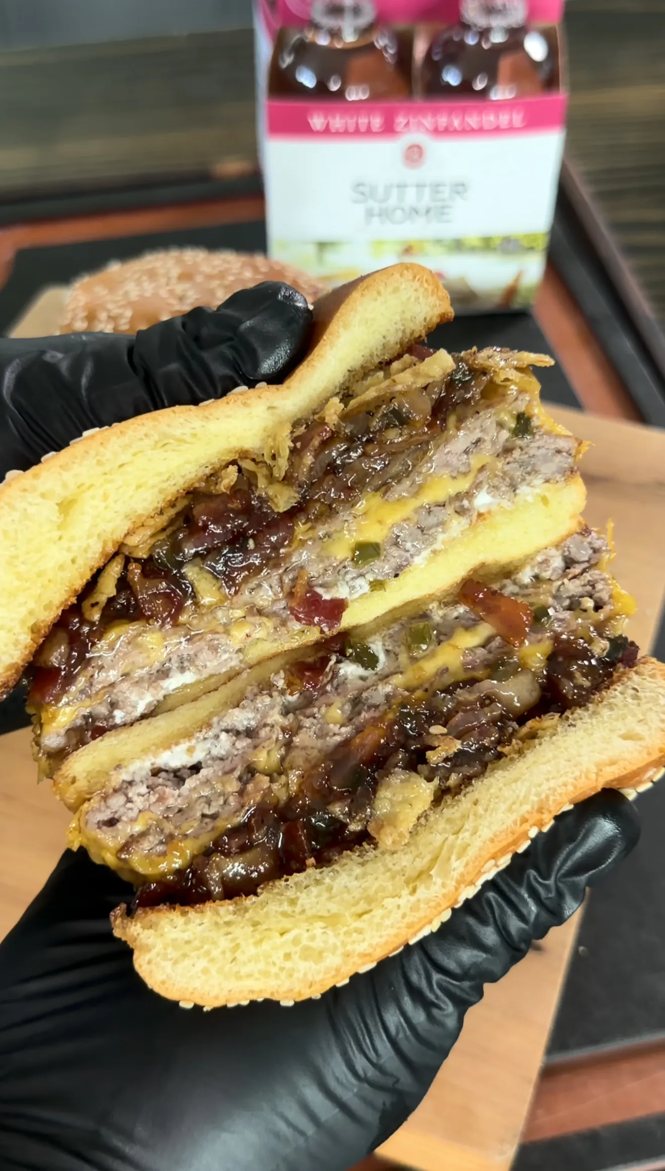 Cross-section of bacon jam smash burger with melted cheese and caramelized onions held in black gloved hands