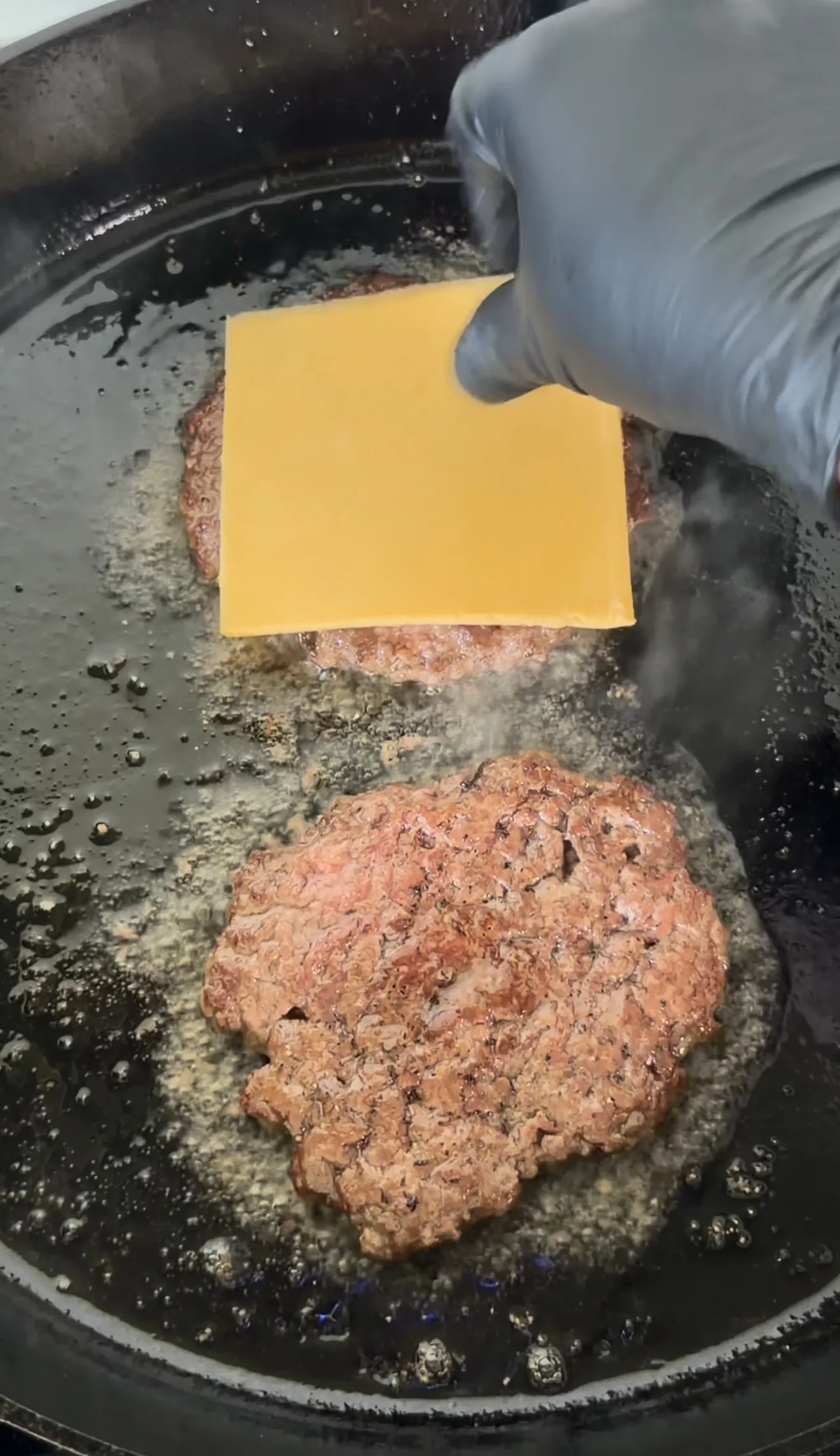 Bacon jam smash burger patties cooking in cast iron with melted cheese on top