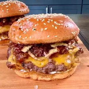 Two bacon jam smash burgers with melted cheese on sesame seed buns, served on a wooden cutting board