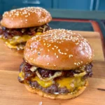 Two bacon jam smash burgers with melted cheese on sesame seed buns, served on a wooden cutting board