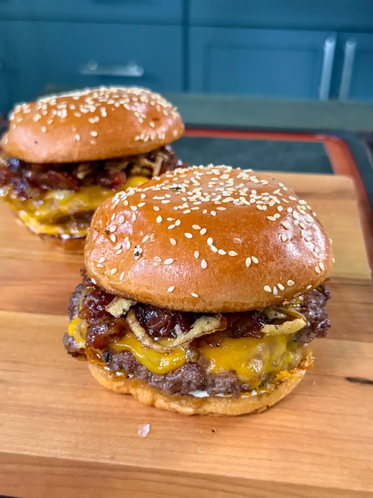 Two bacon jam smash burgers with melted cheese on sesame seed buns, served on a wooden cutting board