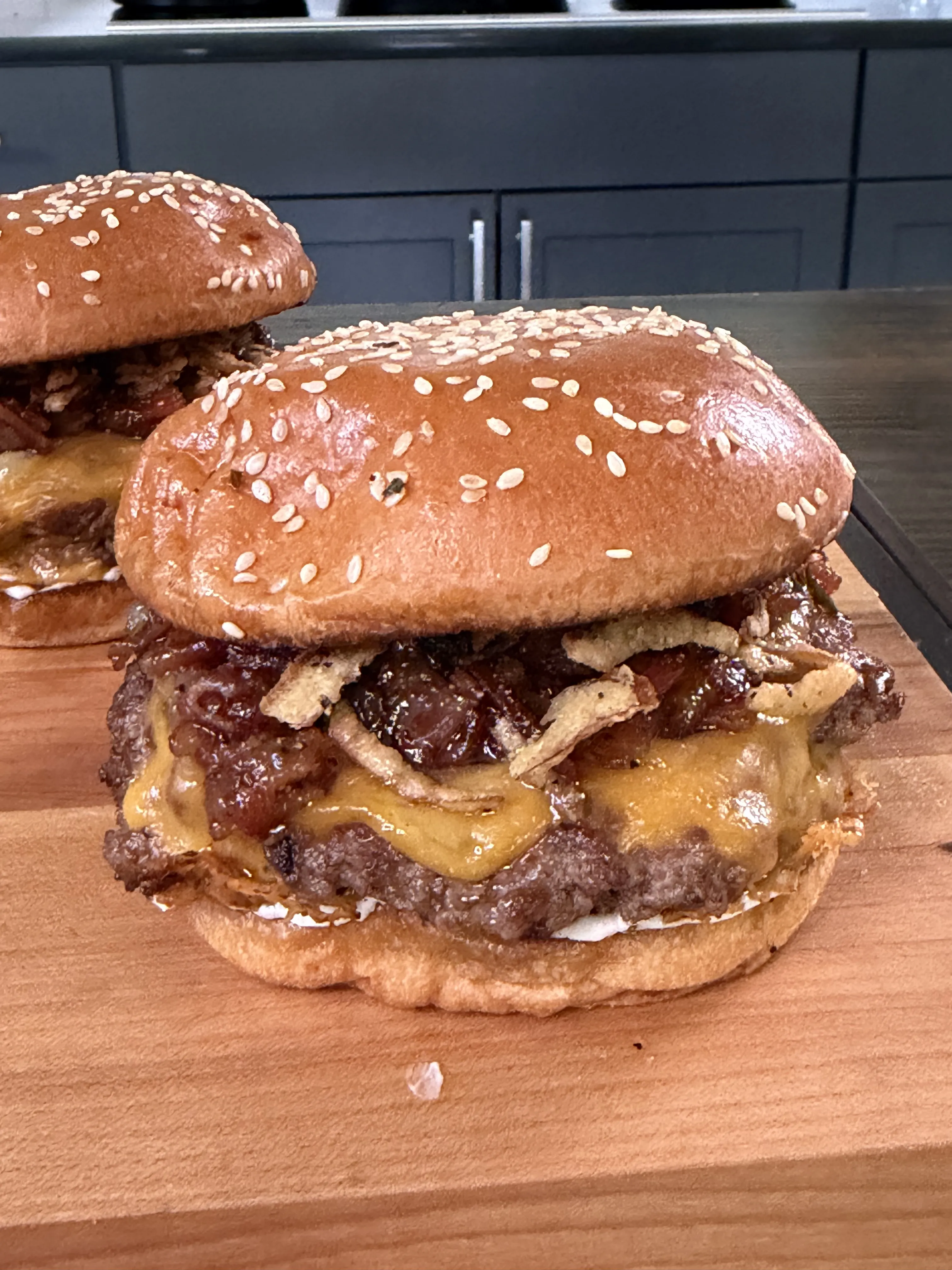 Two bacon jam smash burgers with melted cheese on sesame buns on wooden cutting board
