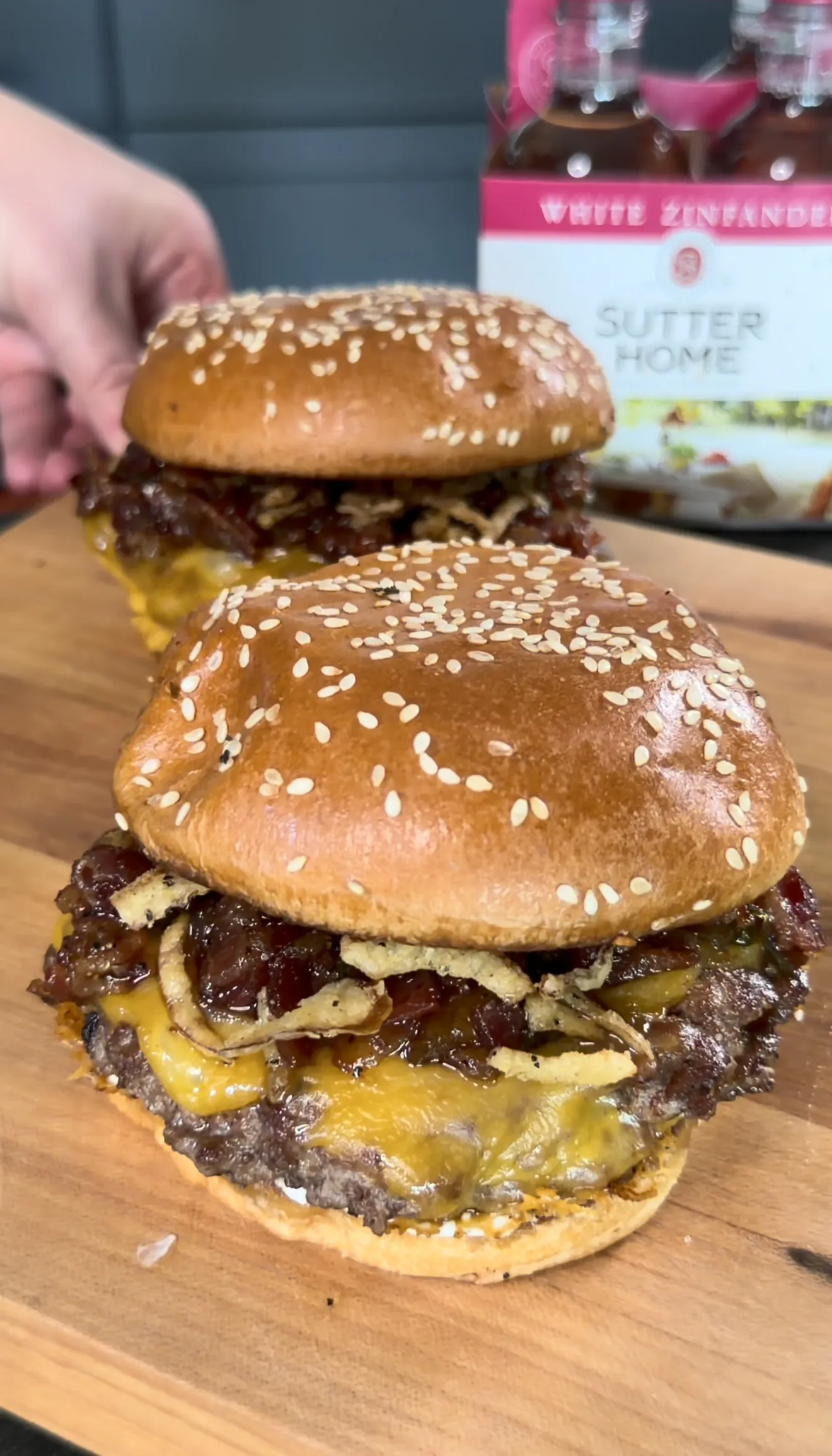 Two stacked bacon jam smash burgers with melted cheese and caramelized onions on wooden board