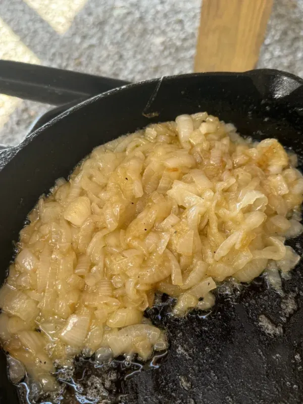 Golden caramelized onions sizzling in a cast iron skillet for smoked Cajun burgers