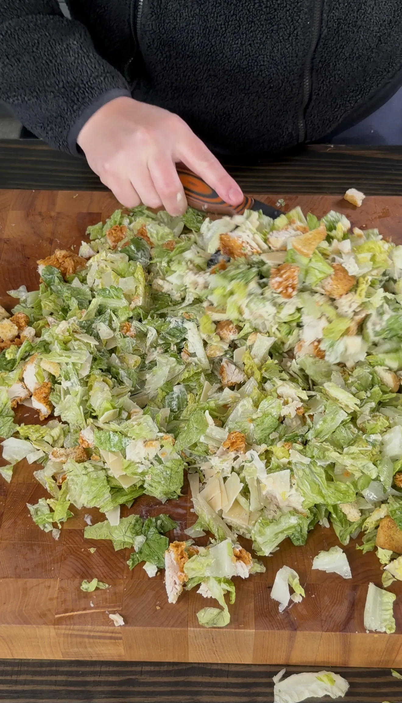 Chopped chicken caesar salad mixture being combined on a cutting board
