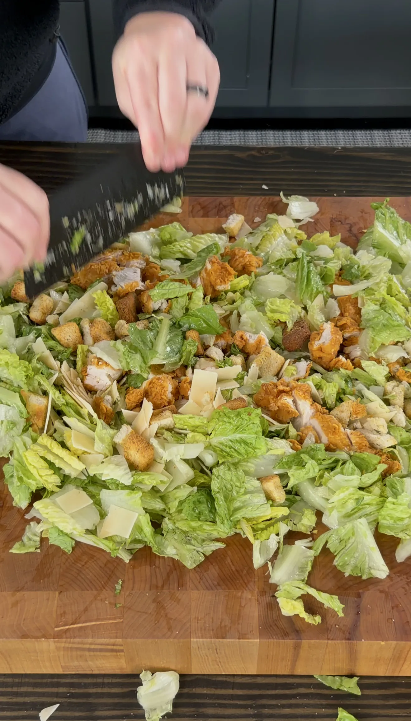 Chopping crispy chicken caesar salad with croutons and parmesan on a cutting board